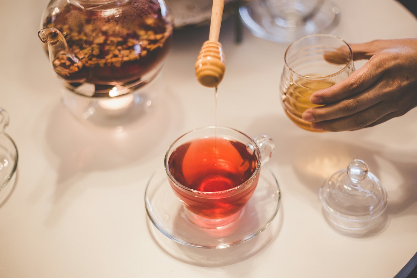 Hand pours golden honey into red herbal tea.