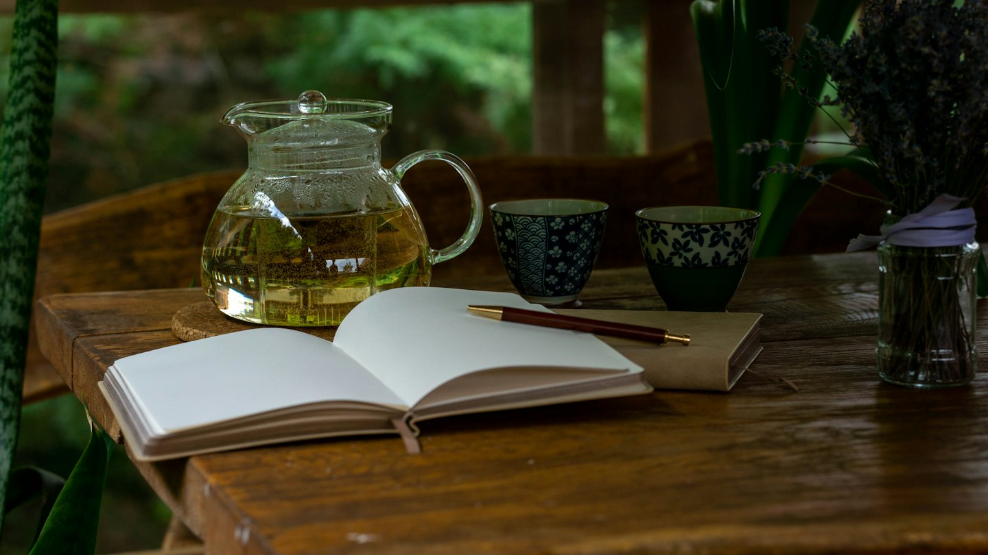 Tea service and notebooks sit on a rustic wooden table.