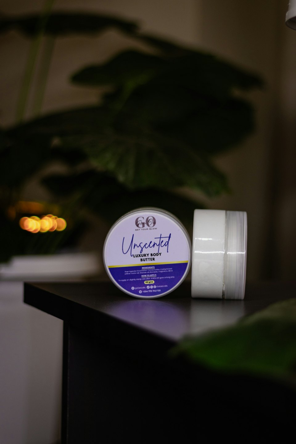 Two jars of body butter resting on a reflective surface.