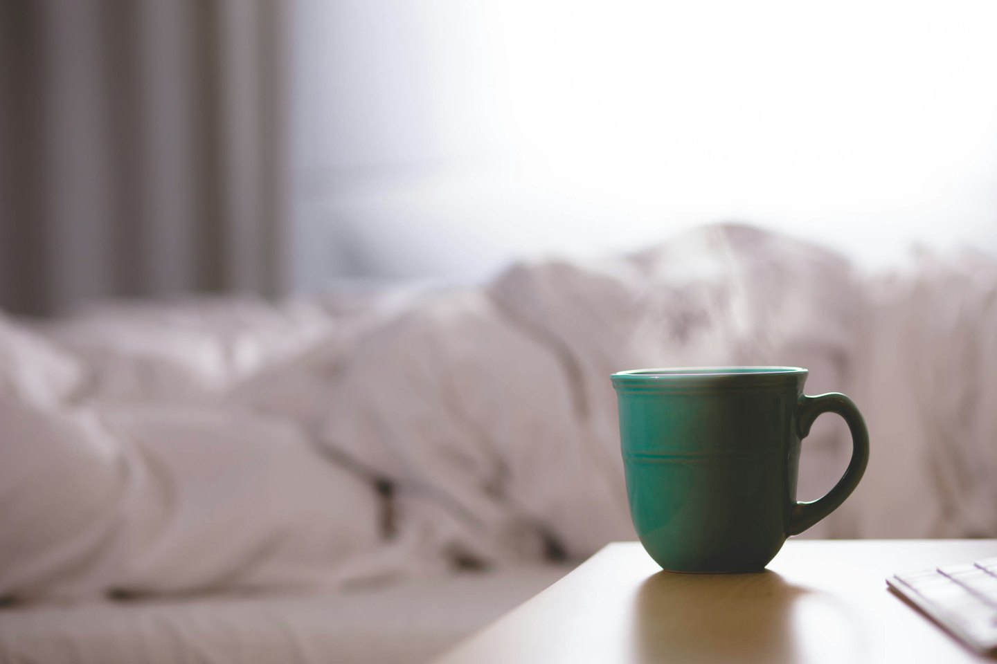 Steaming teal mug on a wooden table near a bed.