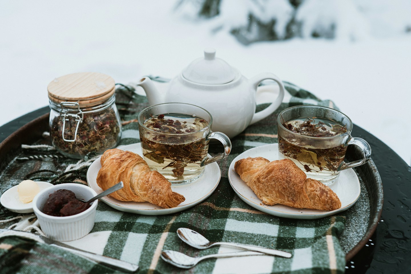 Breakfast of tea and croissants set on a plaid blanket.