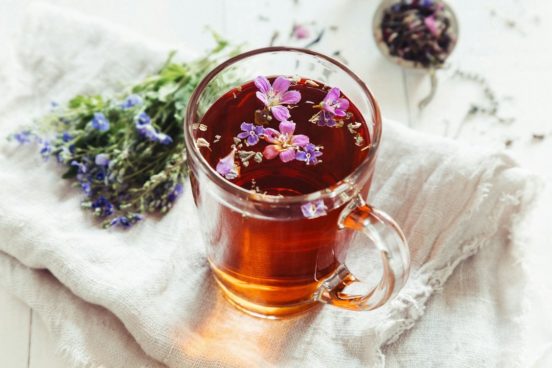 Glass mug of herbal tea with flowers on linen.