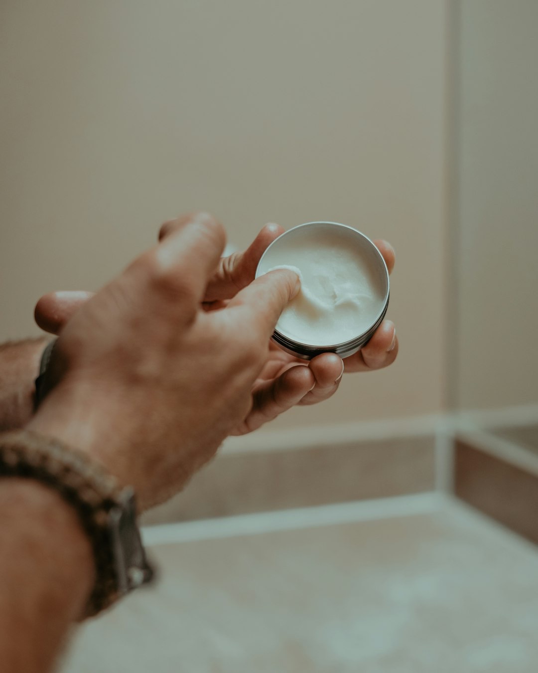 Hands scooping white balm from a small metal tin.